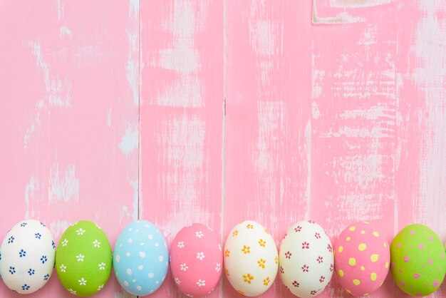 Fila le uova di Pasqua con i fiori di carta variopinti su fondo di legno rosa luminoso.
