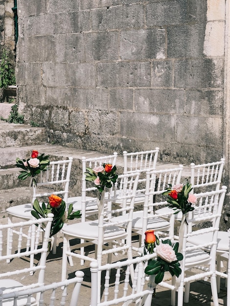 File di sedie bianche decorate con fiori stanno contro un antico muro di pietra