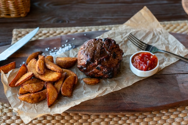 Filet Mignon con patate fritte e salsa di pomodoro su una tavola di legno con posate