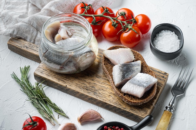 Filetti di aringhe selvatiche in scatola su tagliere di legno su sfondo bianco con erbe e ingredienti