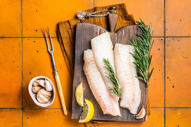 Filetti di pesce di merluzzo crudo baccalà con rosmarino su tavola di legno Sfondo arancione Vista dall'alto