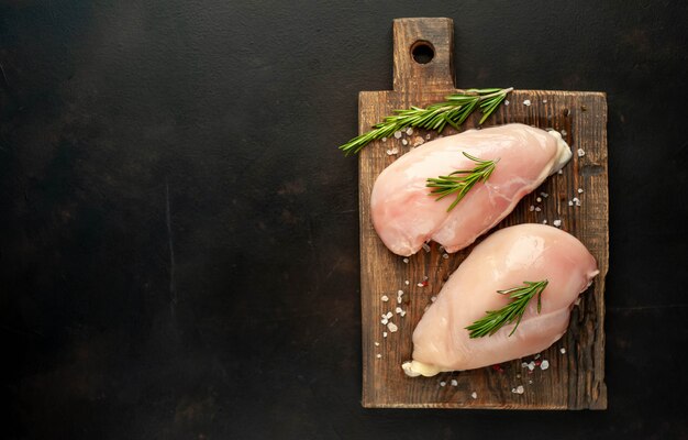 Filetti di petto di pollo crudo, pronti per la cottura su un tagliere di legno con spezie. con spazio copia per il test