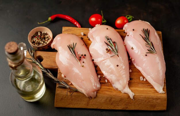 Filetti di petto di pollo crudo, pronti per la cottura su un tagliere di legno con spezie.