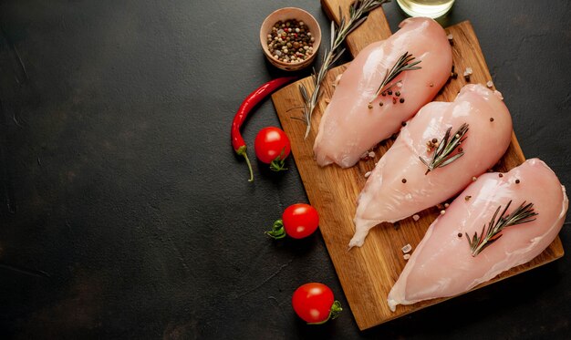 Filetti di petto di pollo crudo, pronti per la cottura su un tagliere di legno con spezie.