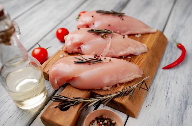 Filetti di petto di pollo crudo, pronti per la cottura su un tagliere di legno con spezie.