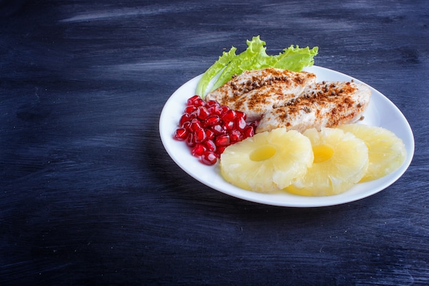 Filetti di pollo fritto con semi di lattuga, ananas e melograno su fondo di legno nero.