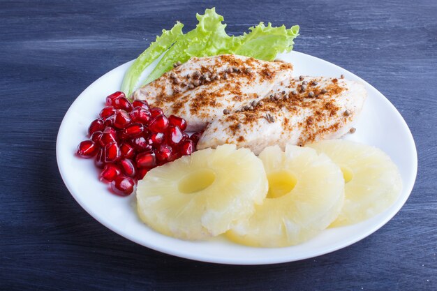 Filetti di pollo fritto con semi di lattuga, ananas e melograno su fondo di legno nero.