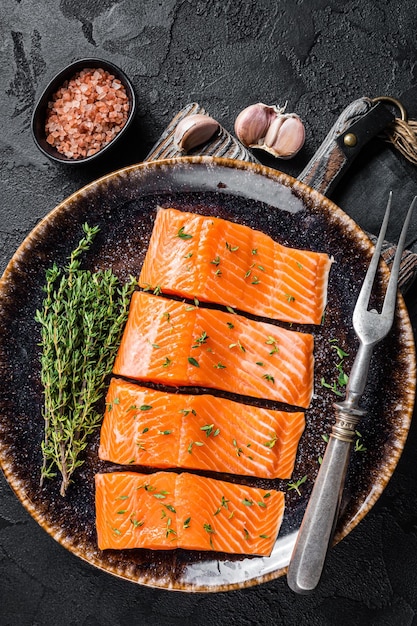 Filetti di salmone, crudo di pesce con timo ed erbe aromatiche. Sfondo nero. Vista dall'alto.