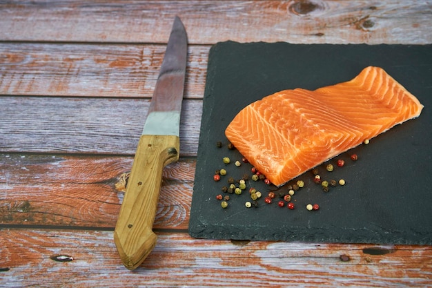 Filetti di salmone fresco su tagliere nero con erbe e spezie