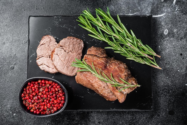 Filetto a fette Bistecca Arrosto di manzo su tavola di marmo con rosmarino Sfondo nero Vista dall'alto