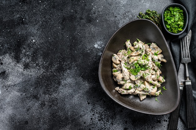 Filetto alla Stroganoff con funghi e prezzemolo fresco in un piatto sul tavolo nero.