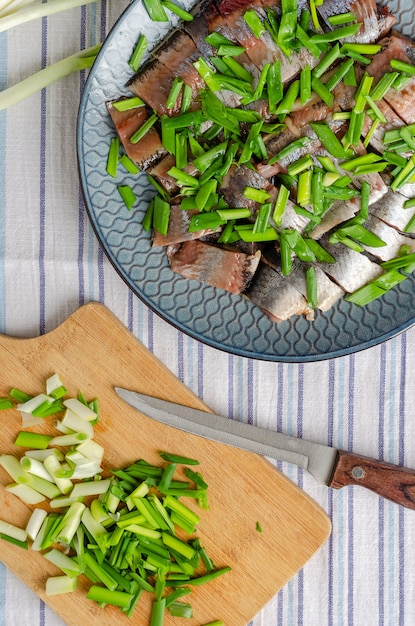 Filetto di aringa tagliato a pezzi con cipolle verdi su piatto blu. Sfondo di legno chiaro