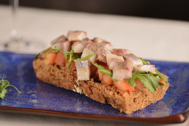 Filetto di aringhe con pomodoro su un pezzo di pane fritto. Su un piatto blu