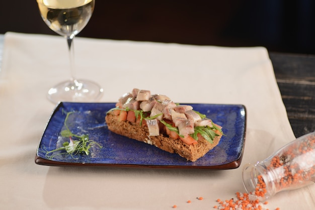 Filetto di aringhe con pomodoro su un pezzo di pane fritto. Su un piatto blu