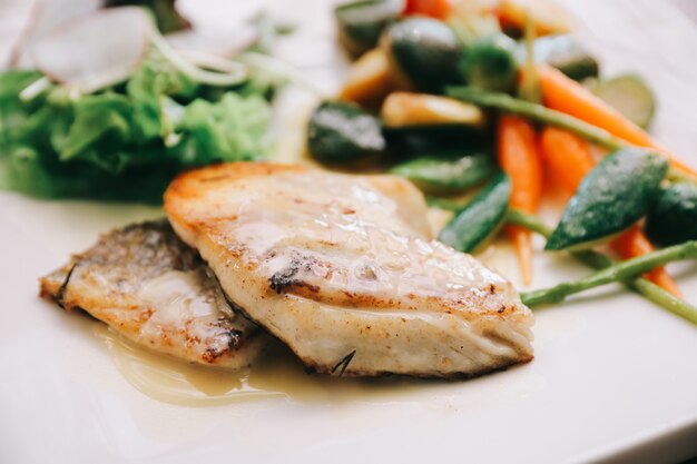 Filetto di branzino con verdure grigliate e insalata sul tavolo di legno