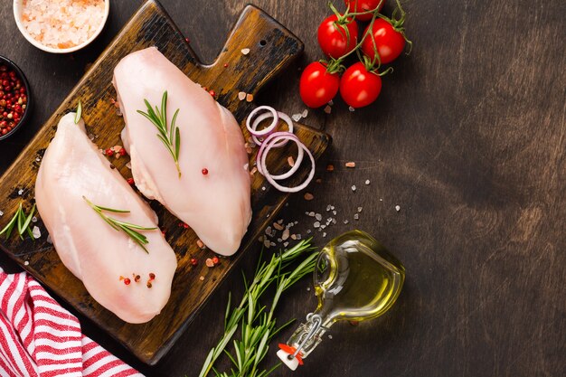 Filetto di carne di pollo crudo fresco con sale, pepe, cipolla e burro su una tavola di legno su un fondo rustico in legno scuro. Vista dall'alto.