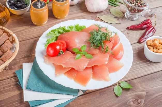 Filetto di carne fresca affettata su un piatto bianco su un fondo di legno scuro.