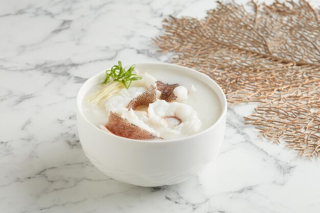 Filetto di Garoupa affettato con Conpoy Congee servito in una ciotola vista laterale su marmo grigio sfondo tradizionale cibo vietnamita