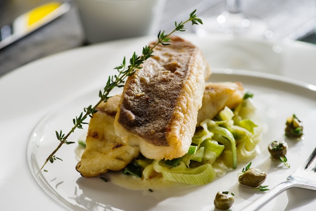 Filetto di ippoglosso su un cuscino di porri in umido sul piatto bianco.