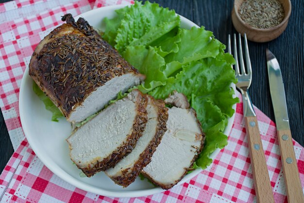 Filetto di maiale al forno in spezie a fette su un piatto bianco con insalata verde.