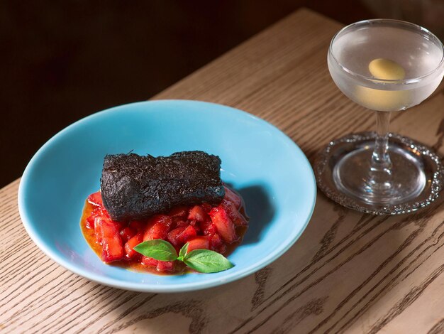 filetto di maiale al forno marinato al nero di seppia con pomodori rossi e basilico su piatto blu