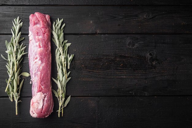 Filetto di maiale crudo. Carne fresca con ingredienti ed erbe per grigliare o cuocere al forno, salvia, set di patate, su sfondo di tavolo in legno nero, vista dall'alto piatta, con copyspace e spazio per il testo