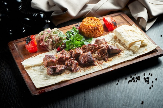 Filetto di manzo alla griglia con bulgur e verdure guarnito su una tavola di legno. Kebab turco. Primo piano, messa a fuoco selettiva