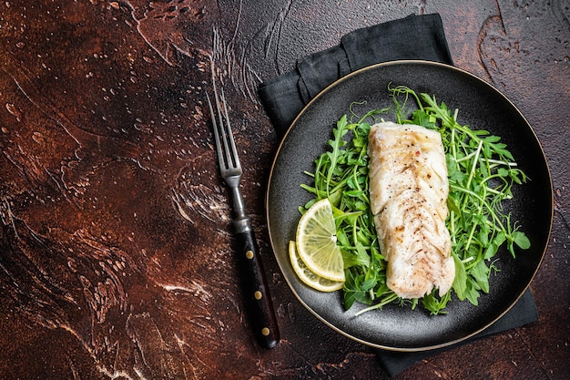 Filetto di merluzzo alla griglia servito con insalata verde in un piatto Sfondo scuro Vista dall'alto Copia spazio