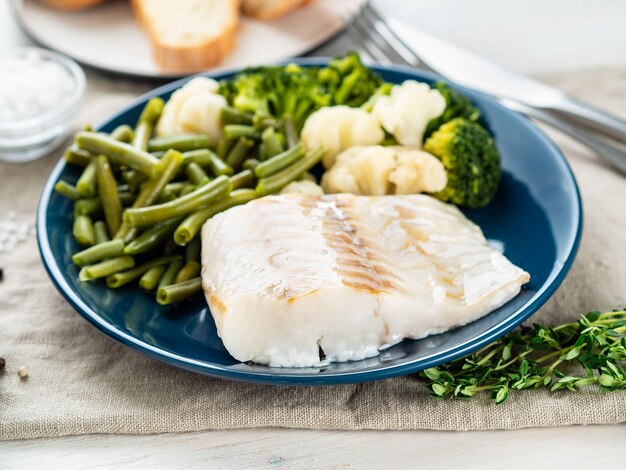 Filetto di merluzzo bollito con verdure su piatto blu tavola di legno grigia vista laterale dieta sana