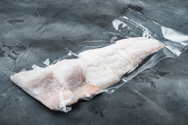 Filetto di pesce bianco di eglefino in confezione di plastica per il mercato, su sfondo grigio con spazio di copia per il testo