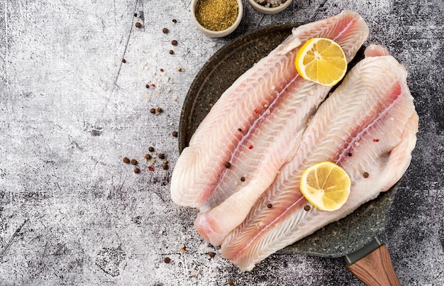 Filetto di pesce pangasio crudo con limone e spezie su fondo di cemento