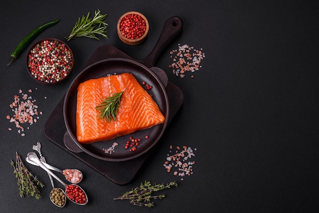 Filetto di pesce salmone rosso crudo con sale spezie ed erbe aromatiche su uno sfondo di cemento scuro