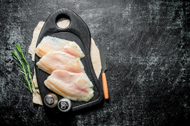 Filetto di pesce su un tagliere con un coltello spezie e rosmarino