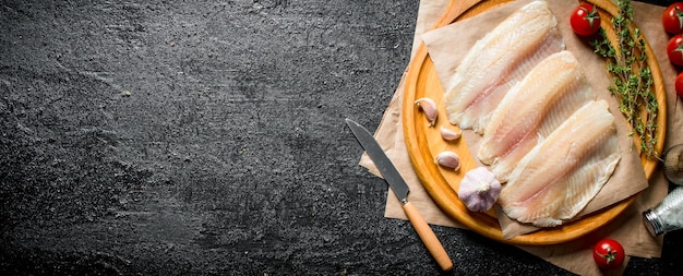 Filetto di pesce su un tagliere rotondo con un coltello timo pomodori e spezie