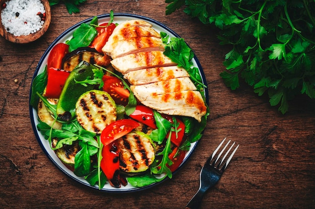 Filetto di petto di pollo alla griglia e insalata di verdure con paprika zucchine melanzane pomodori freschi ed erbe miste Tavolo in legno rustico sfondo vista dall'alto