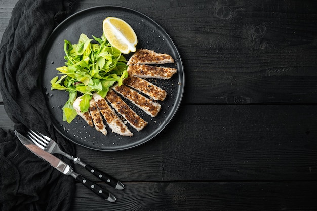 Filetto di petto di pollo sbriciolato alla griglia, su un tavolo di legno nero, vista dall'alto