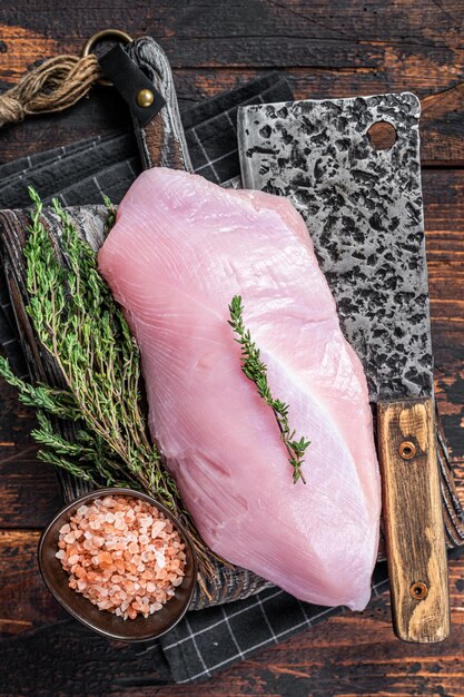 Filetto di petto di tacchino crudo su una tavola da macellaio in legno con mannaia. Fondo in legno scuro. Vista dall'alto.