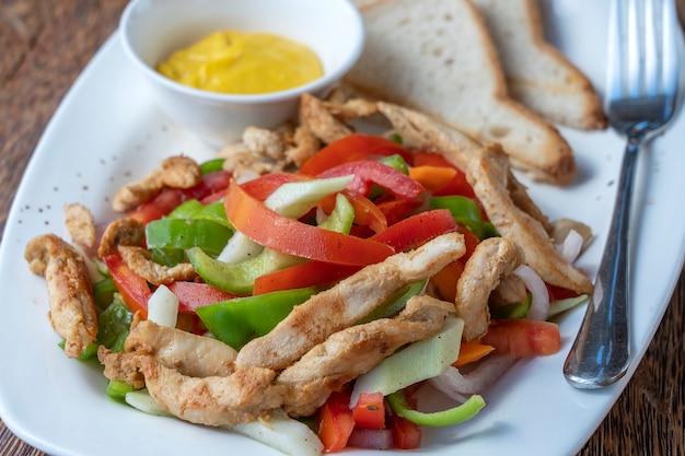 Filetto di pollo arrosto con verdure e pane su un piatto bianco, primo piano