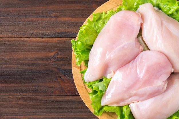 Filetto di pollo crudo e insalata verde su un tagliere rotondo su un fondo di tavolo in legno.