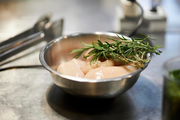 filetto di pollo crudo e ramo di rosmarino in una ciotola di metallo sul primo piano del tavolo della cucina