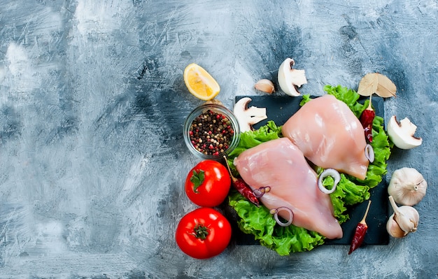 Filetto di pollo crudo sul tagliere con spezie ed erbe aromatiche.