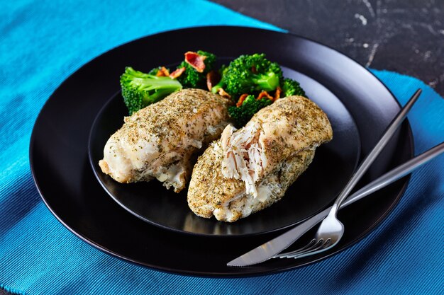 Filetto di pollo magro al forno con condimento ranch servito su un piatto nero con broccoli e pancetta