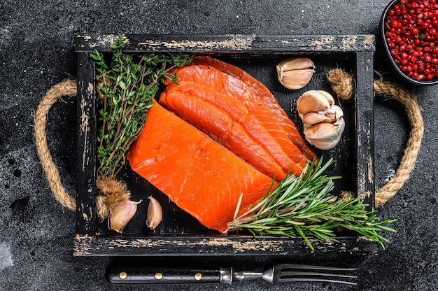 Filetto di salmone affumicato a fette in un vassoio di legno con erbe aromatiche.