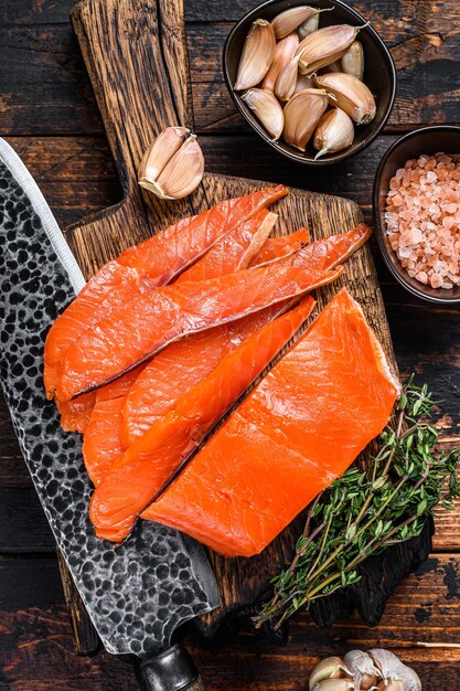 Filetto di salmone affumicato a fette su un tagliere di legno con erbe aromatiche. Fondo in legno scuro. Vista dall'alto.