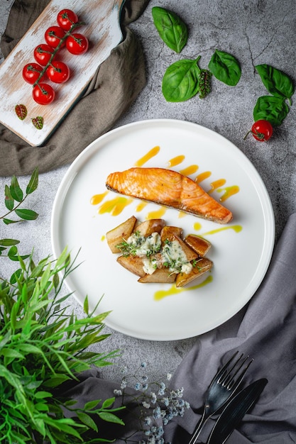 Filetto di salmone al forno con patate rustiche su pere dolci ripiene di formaggio nobile con salsa di arance mature in un piatto su un tavolo di pietra grigia. Menù Ristorante