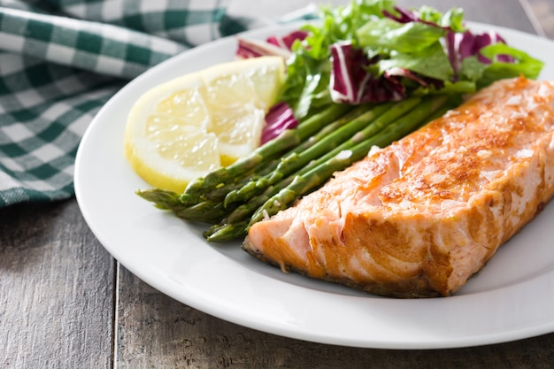 Filetto di salmone alla griglia con asparagi e insalata nel piatto sul tavolo di legno