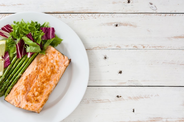 Filetto di salmone alla griglia con asparagi e insalata nel piatto sulla vista del piano del tavolo in legno bianco