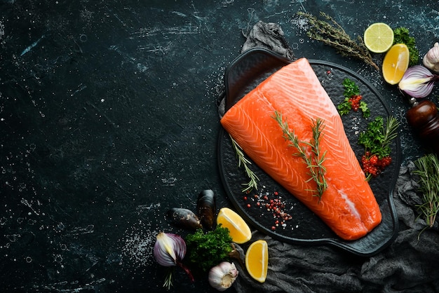 Filetto di salmone crudo al rosmarino su un piatto di pietra nero. Su uno sfondo scuro. Disposizione piatta.