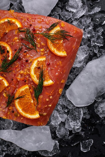 Filetto di salmone crudo con fette di arancia su pezzi di ghiaccio su fondo nero