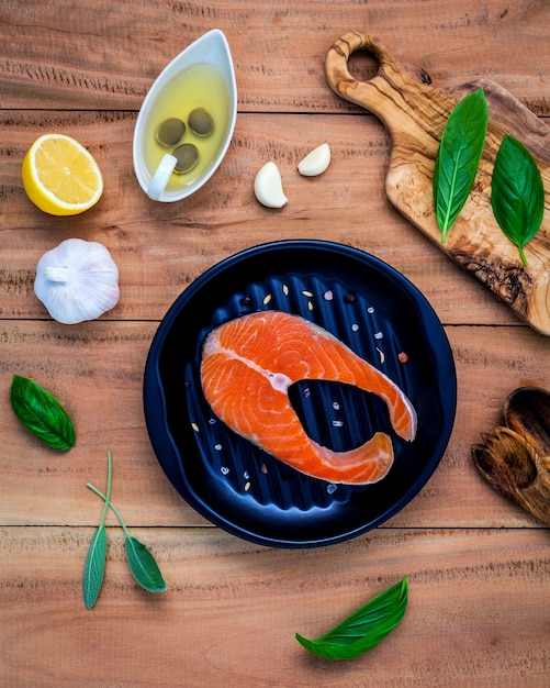 Filetto di salmone crudo con ingredienti su fondo di legno.